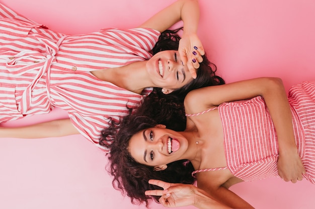 Meninas jovens e atraentes, com lindo cabelo bronzeado e encaracolado escuro, sorriem sinceramente e mostram o símbolo da paz.