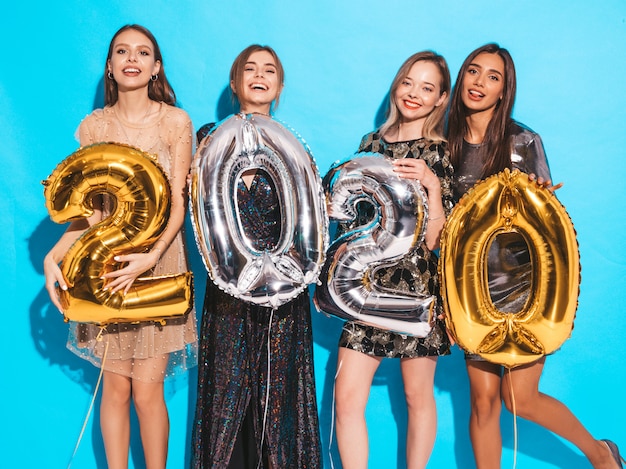 Meninas lindas felizes em elegantes vestidos de festa sexy segurando balões de ouro e prata 2020