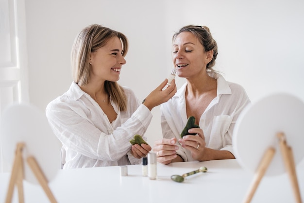 Meninas loiras caucasianas sorridentes estão experimentando um novo produto cosmético enquanto estão sentados à mesa no estúdio. Beleza e cuidados pessoais, conceito de cuidados com a pele e rosto