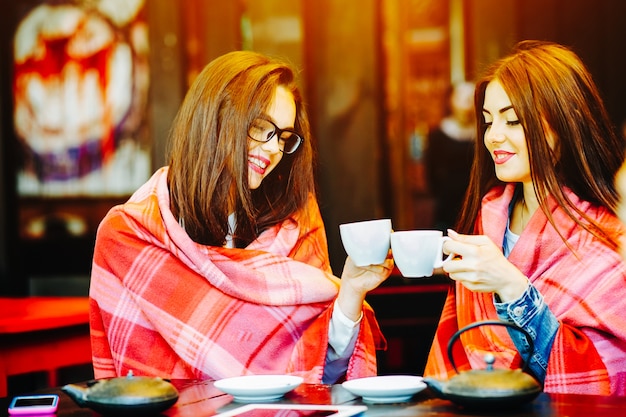 Meninas que brindam com copos de café coberto com um cobertor