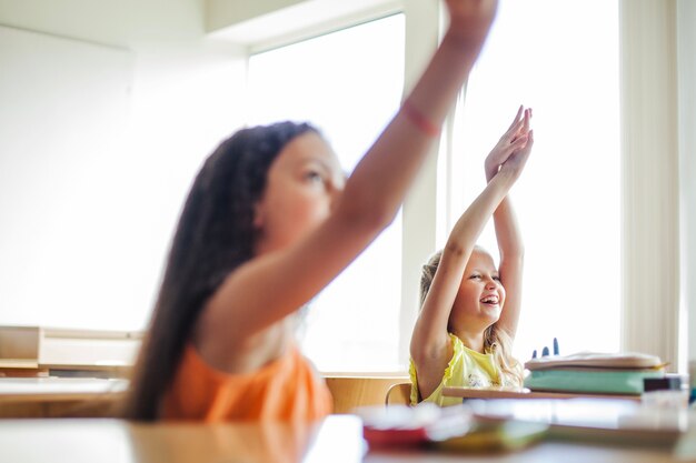 Meninas sentadas nas mesas da escola levantando as mãos