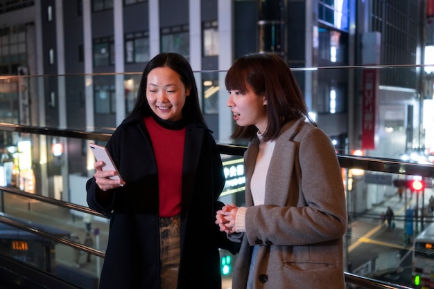 Meninas sorridentes de tiro médio com telefone noturno