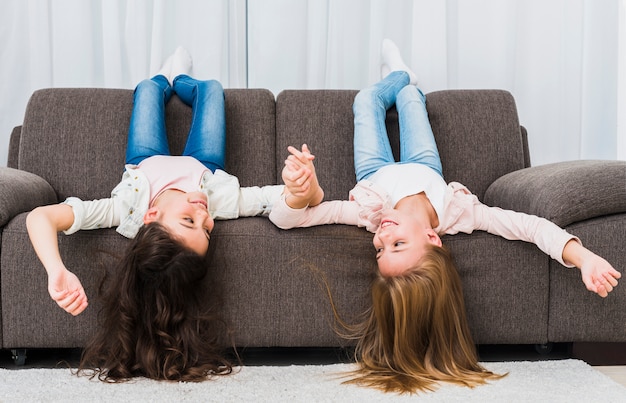 Foto grátis meninas sorridentes deitado no sofá de cabeça para baixo, segurando a mão do outro na sala de estar