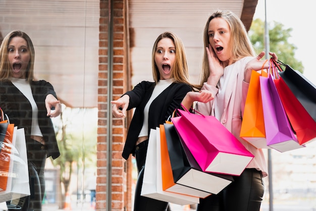 Meninas surpreendidas com sacos de compras, olhando para a janela