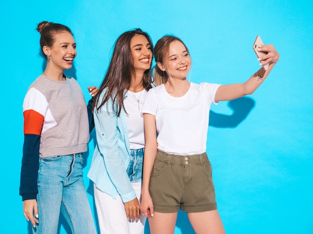 Meninas, tirando fotos de auto-retrato de selfie no smartphone. modelos posando perto de parede azul no estúdio, fêmea, mostrando emoções de rosto positivo