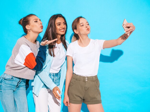 Meninas tirando fotos de auto-retrato de selfie no smartphone. Modelos posando perto de parede azul no estúdio.