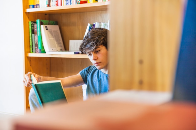 Menino adolescente, leitura, atrás de, estante