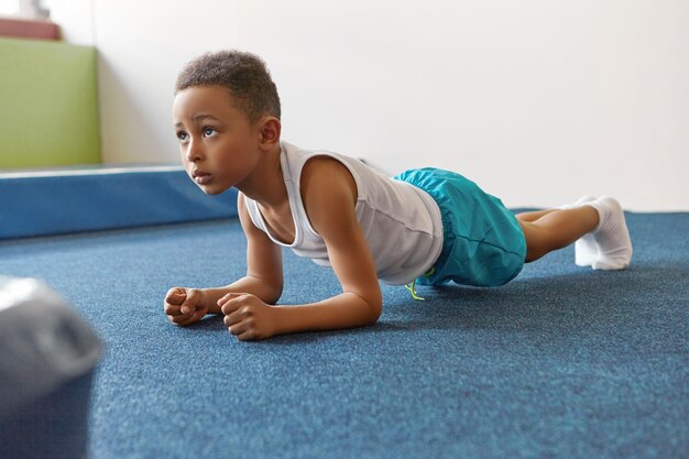 Menino afro-americano autodeterminado, vestido com roupas esportivas, praticando ginástica