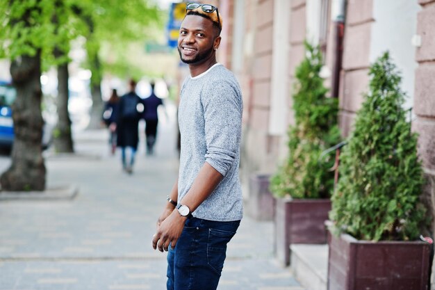 Menino afro-americano elegante na camisola cinza e óculos de sol pretos posou na rua Cara negro na moda