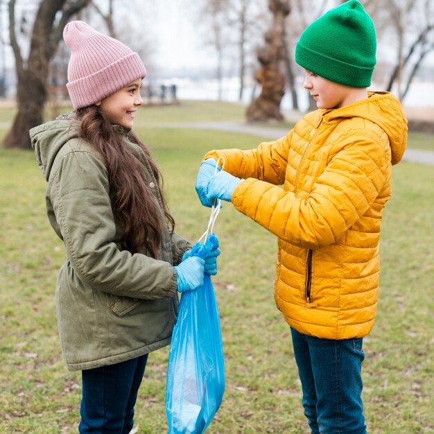Menino ajuda menina fazendo um nó no saco de plástico