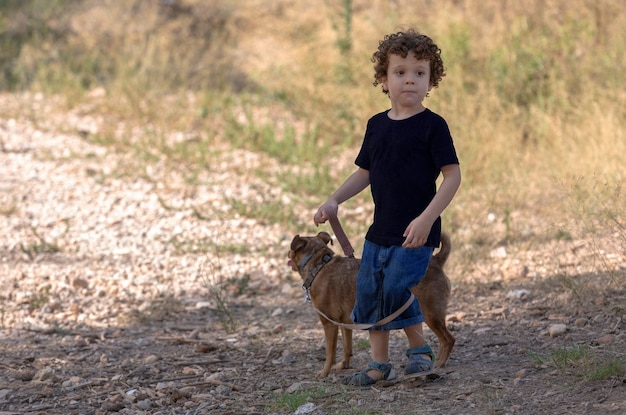 Menino andando e brincando com seu cachorrinho na floresta, longe do perigo da cidade