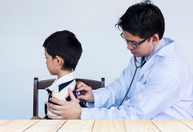 Menino asiático doente sendo examinado pelo médico sobre fundo branco