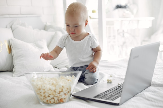 Menino bonitinho brincando com um laptop em uma cama