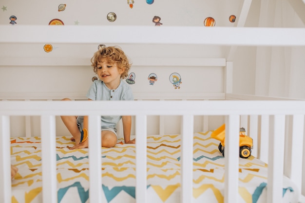 Menino bonitinho se divertindo na cama em forma de uma casa