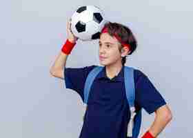 Foto grátis menino bonito e esportivo satisfeito olhando em linha reta tocando a cabeça com uma bola de futebol