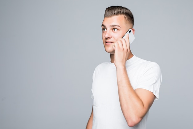 Menino bonito em camiseta branca falando em seu telefone celular isolado na parede branca