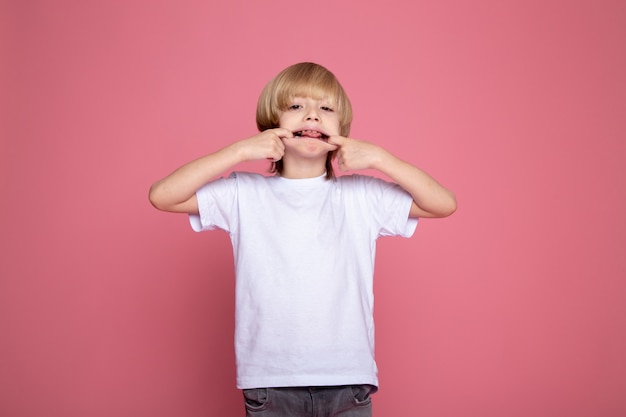 Menino bonito, fazendo expressões faciais engraçadas em t-shirt branca e jeans cinza retrato de menino criança adorável bonito na mesa-de-rosa