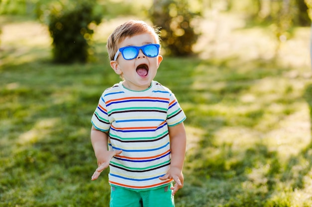 Menino bonito parece surpreso no jardim de verão em óculos de sol brilhantes.
