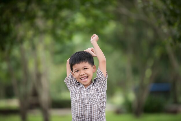 Menino bonito pequeno que aprecia levantando as mãos com natureza sobre o fundo borrado da natureza.