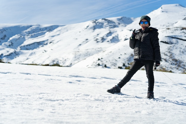 Menino caucasiano feliz vestindo roupas quentes na montanha de neve no inverno