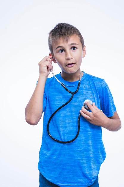 Foto grátis menino chocado ouvir seu batimento cardíaco com estetoscópio no fundo branco