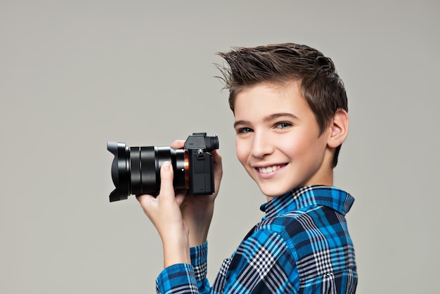 Menino com câmera fotográfica tirando fotos. Retrato do menino caucasiano com uma câmera digital nas mãos