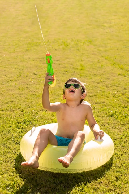 Foto grátis menino com chapéu e óculos de sol, brincando com pistola de água