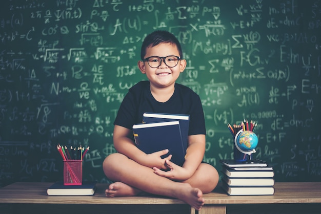 menino com livros sentado perto de lousa verde