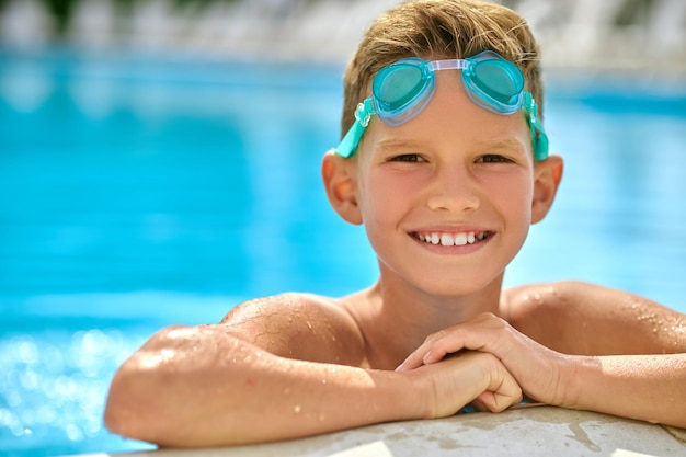 Menino com óculos sorrindo para a câmera na piscina