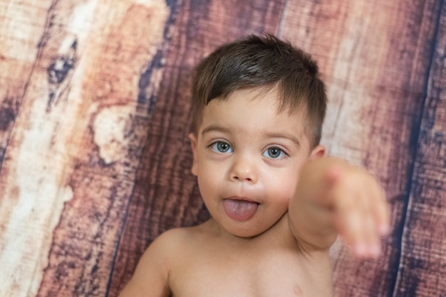 Menino com olhos azuis deitado na parede de madeira com a língua para fora