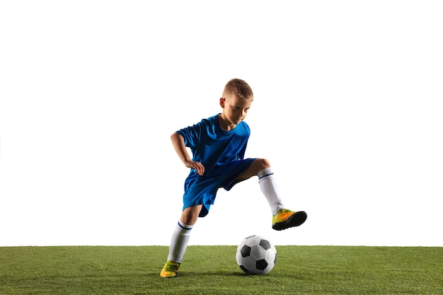 Menino como um jogador de futebol ou futebol americano no sportwear, fazendo uma finta ou um chute com a bola para um gol no fundo branco do estúdio. Ajuste o menino brincando em ação, movimento, movimento no jogo.