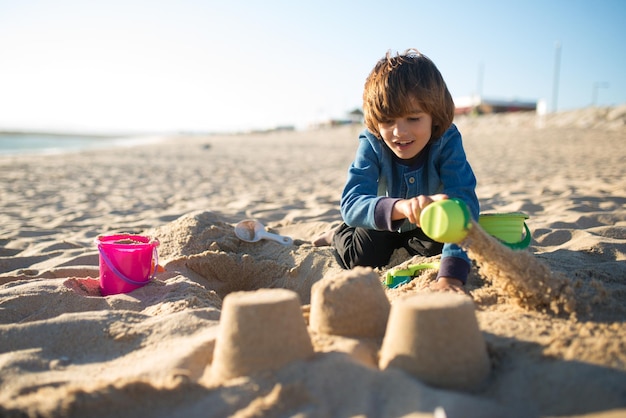 Menino construindo castelo de areia. Aluno brincando na praia nas férias de verão