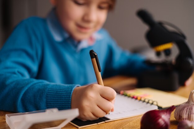 Menino da primeira série estudando em casa usando microscópio