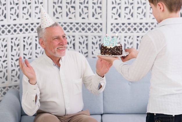 Foto grátis menino, dar, surpreendido, bolo aniversário, para, seu, feliz, avô, sentar sofá