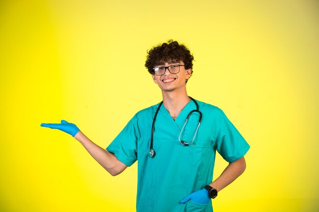 Menino de cabelo encaracolado com uniforme médico e máscaras de mão mostrando algo.