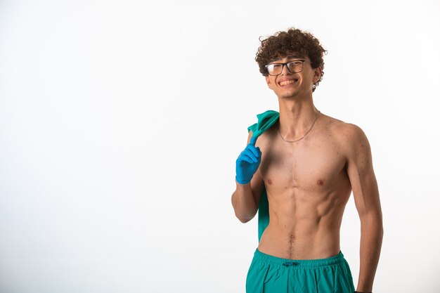 Menino de cabelo encaracolado em óculos de optique, mostrando os músculos do corpo após o treino.