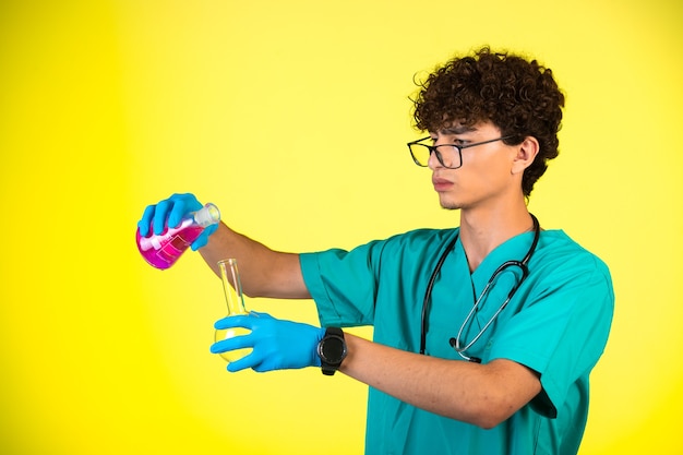 Foto grátis menino de cabelo encaracolado em uniforme médico e máscaras de mão, fazendo reação química com frascos.