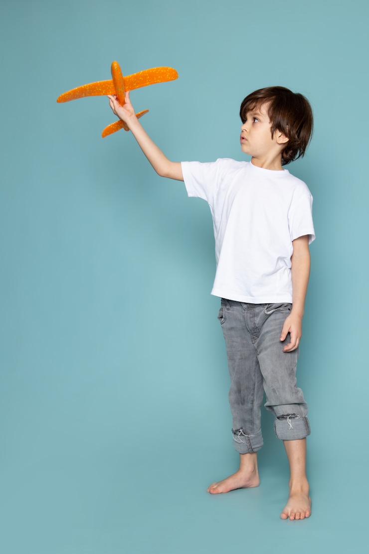 Foto grátis menino de criança vista frontal em camiseta branca segurando o avião de brinquedo laranja azul