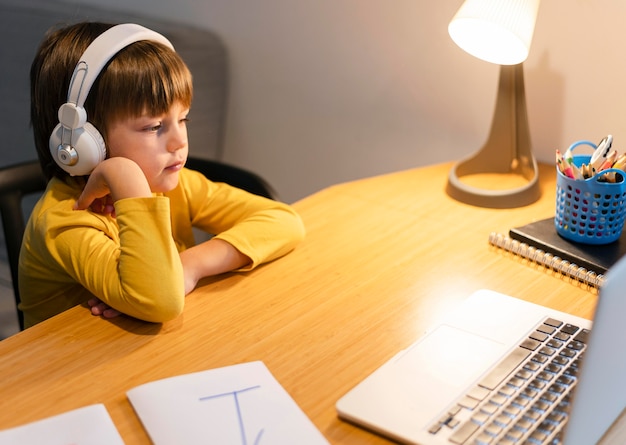 Menino de escola com camisa amarela assistindo aulas virtuais de alta vista