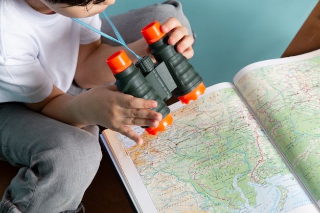 Menino de vista frontal, olhando através do mapa com binóculos