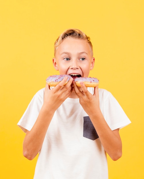 Menino de vista frontal tentando comer dois donuts de uma só vez