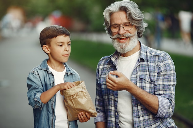 Menino e avô estão caminhando no parque. Velho brincando com o neto. As pessoas comem pipoca.