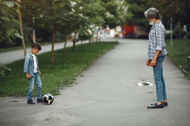 Menino e avô estão caminhando no parque. Velho brincando com o neto. Família brincando com uma bola.