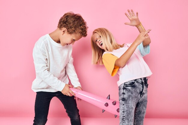 Menino e menina com bastão de brinquedo brincando com um fundo rosa