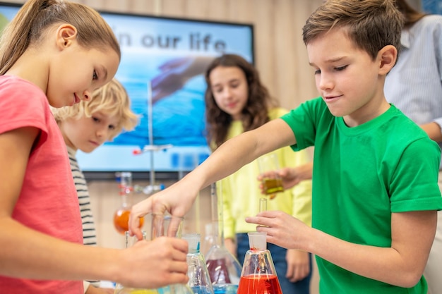 Menino e menina de lado para a câmera fazendo experimento de química