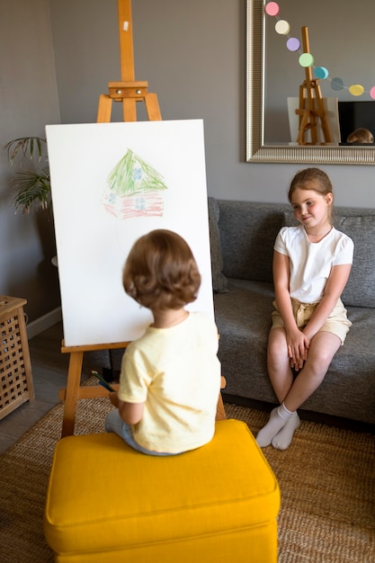 Menino e menina desenhando juntos em casa usando cavalete