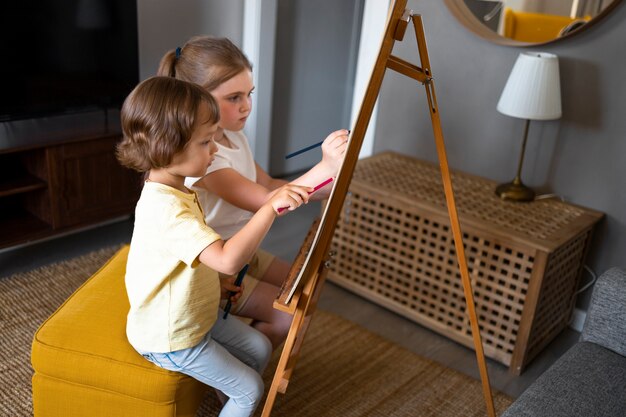 Menino e menina desenhando juntos em casa usando cavalete