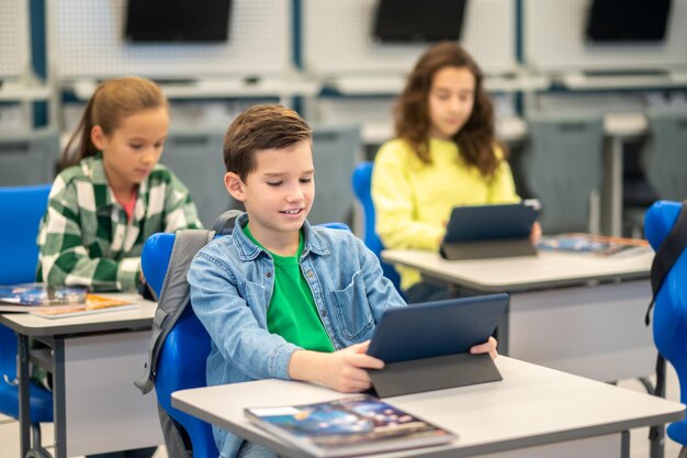 Menino e meninas sentados na mesa olhando para tablet