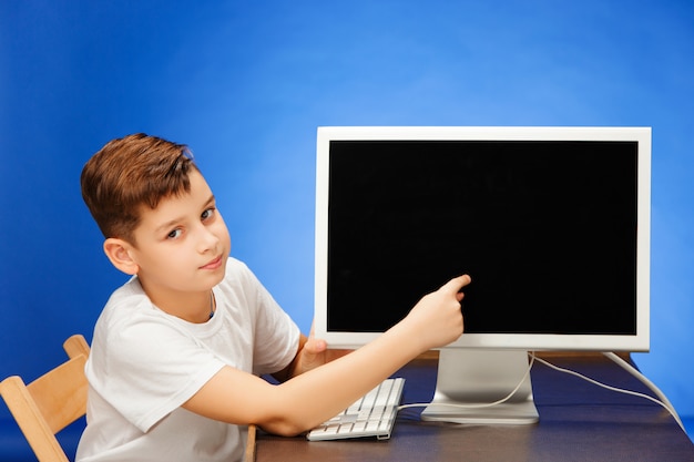 Menino em idade escolar, sentado com o laptop monitor no estúdio