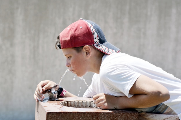 Menino em um boné de beisebol bebe água com sede de um bebedor